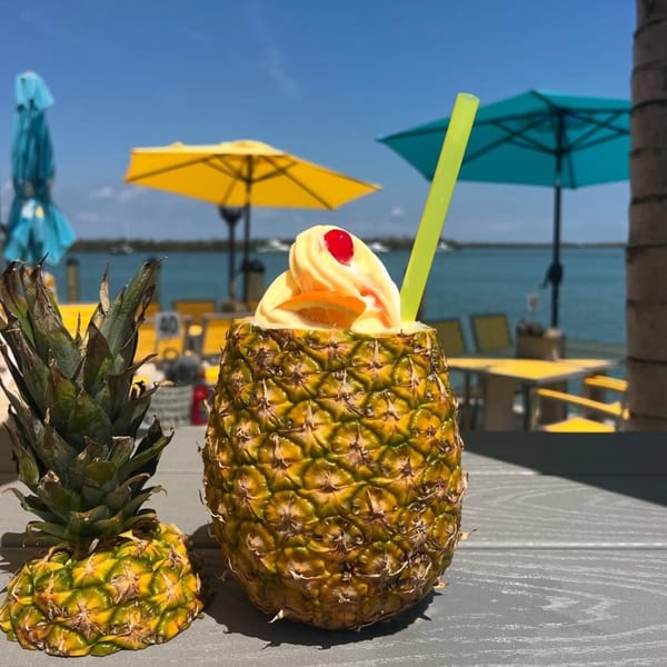 Pineapple Dole Whip with a cherry and orange slice, with beach umbrellas and ocean in the background.