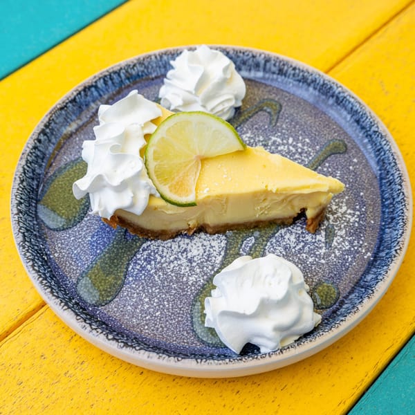 A slice of key lime pie with whipped cream and a lime wedge on a blue plate.