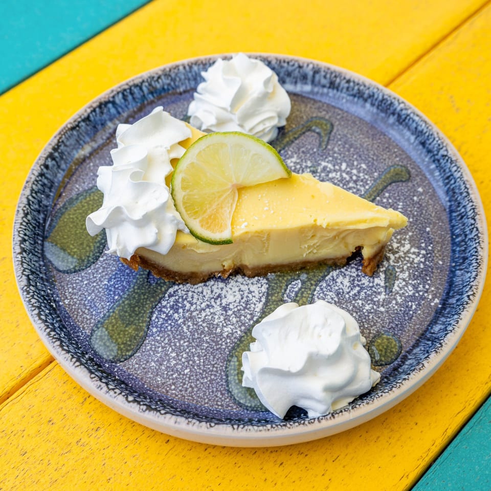A slice of key lime pie with whipped cream and a lime wedge on a blue plate.