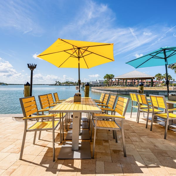 Outdoor dining area with yellow tables and chairs under umbrellas, next to a body of water.