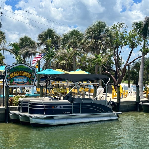 Beachcomber Trading Post sign, pontoon boat, and outdoor seating area with palm trees.
