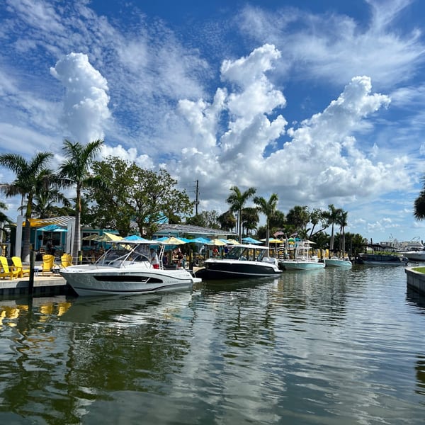 Boats docked at Beachcomber Trading Post Restaurant, with palm trees and blue sky with clouds.