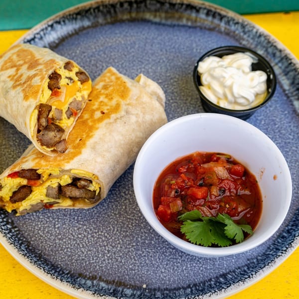 Two breakfast burritos filled with eggs, sausage, and cheese, served with salsa and sour cream.