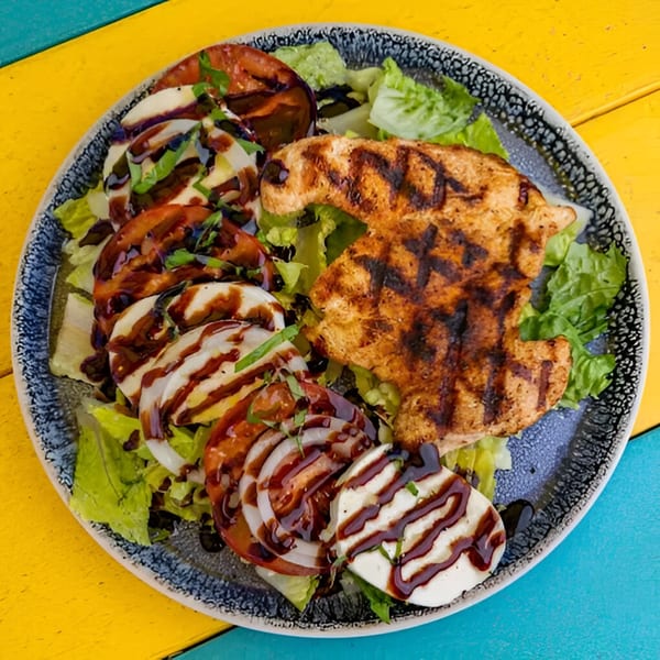 Grilled chicken and caprese salad with balsamic glaze on a blue and white plate.