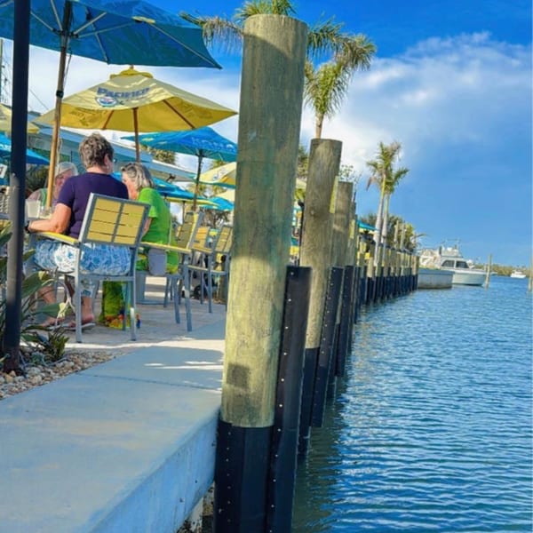 Diners seated under blue and yellow umbrellas at Beachcomber Trading Post Restaurant's waterfront patio.
