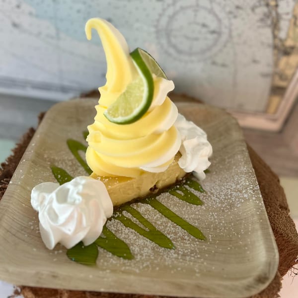 A slice of key lime pie topped with yellow soft serve, whipped cream, and a lime wedge.