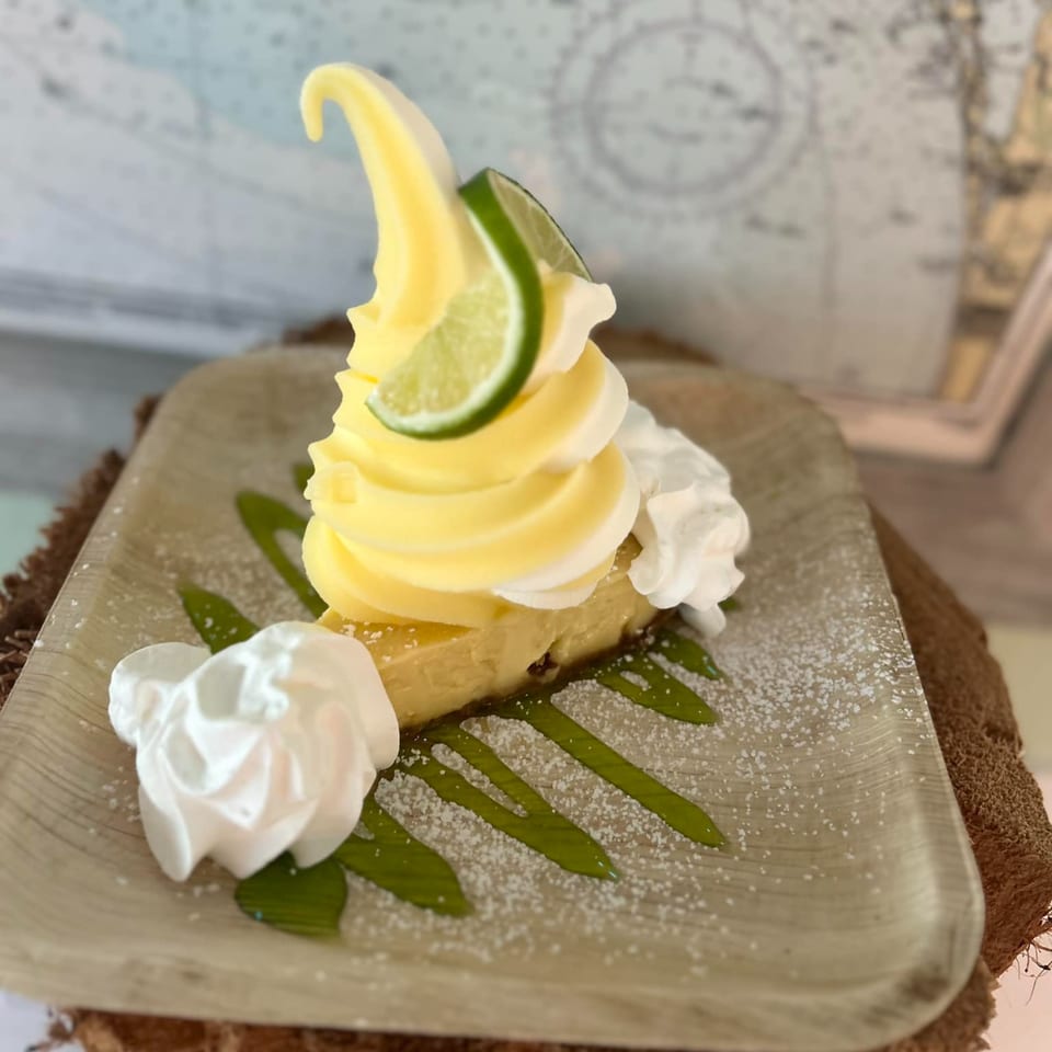 A slice of key lime pie topped with yellow soft serve, whipped cream, and a lime wedge.