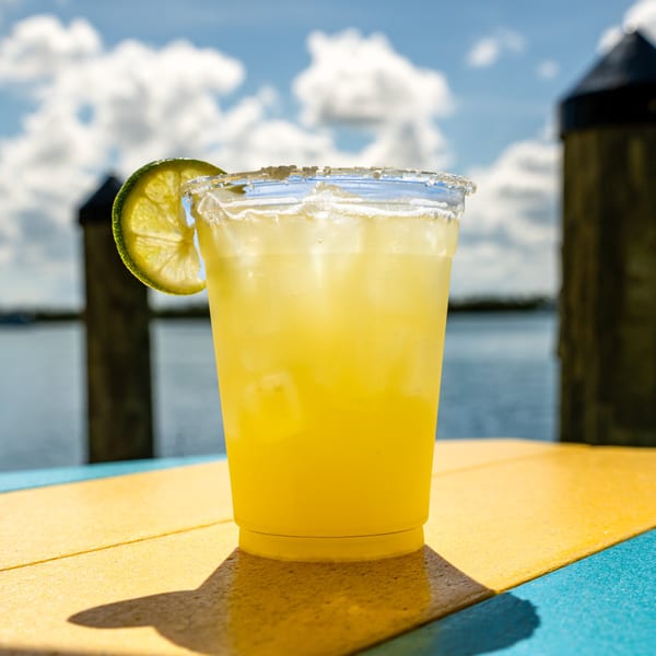 A Beachcomber Trading Post margarita with a lime wedge and salted rim, on a dock overlooking water.