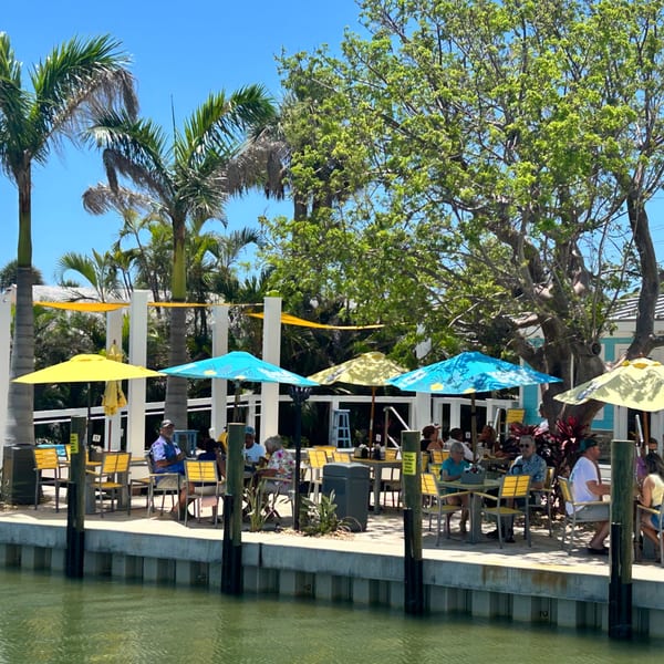 Diners enjoy outdoor seating under colorful umbrellas at Beachcomber Trading Post Restaurant, overlooking the water.