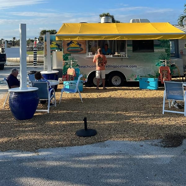 A Beachcomber Trading Post food truck with a yellow awning, outdoor seating, and customers.