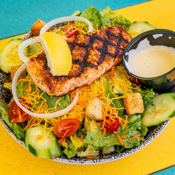 Grilled salmon salad with lettuce, tomatoes, cucumbers, onions, shredded cheese, croutons, and dressing.