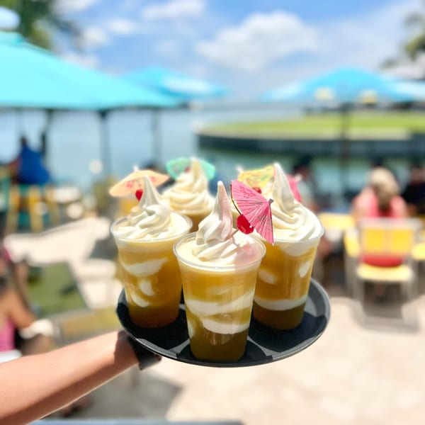 Tray of five pineapple Dole Whip drinks with umbrellas and cherries, served at an outdoor restaurant.