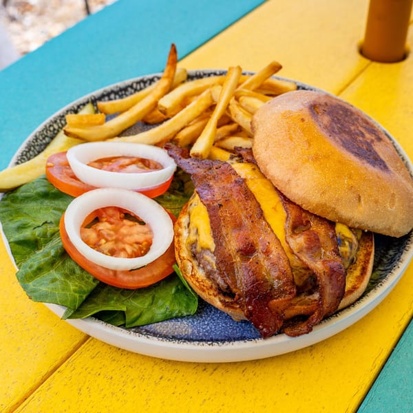A bacon cheeseburger with fries, lettuce, tomato, and onion on a colorful table.