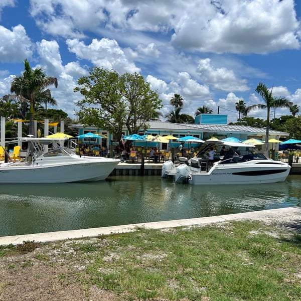 Two boats docked at Beachcomber Trading Post Restaurant, with outdoor seating under colorful umbrellas.