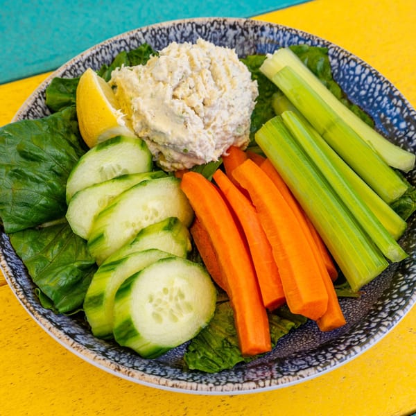 A plate of tuna salad with lettuce, cucumber slices, carrot sticks, celery sticks, and a lemon wedge.